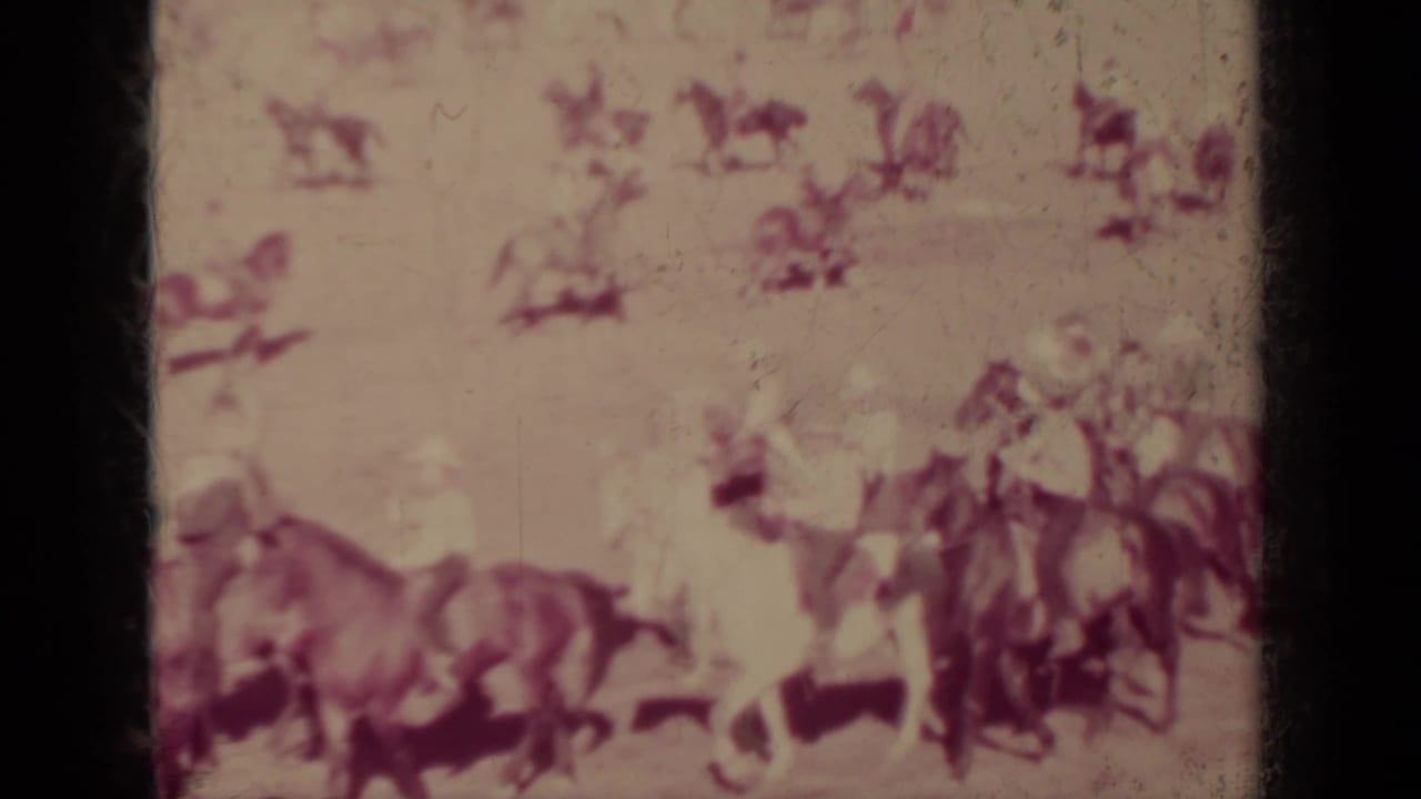 Riders on horseback appear in loose formation during the Klamath, California outdoor equestrian event, with distant spectators and riders behind them.