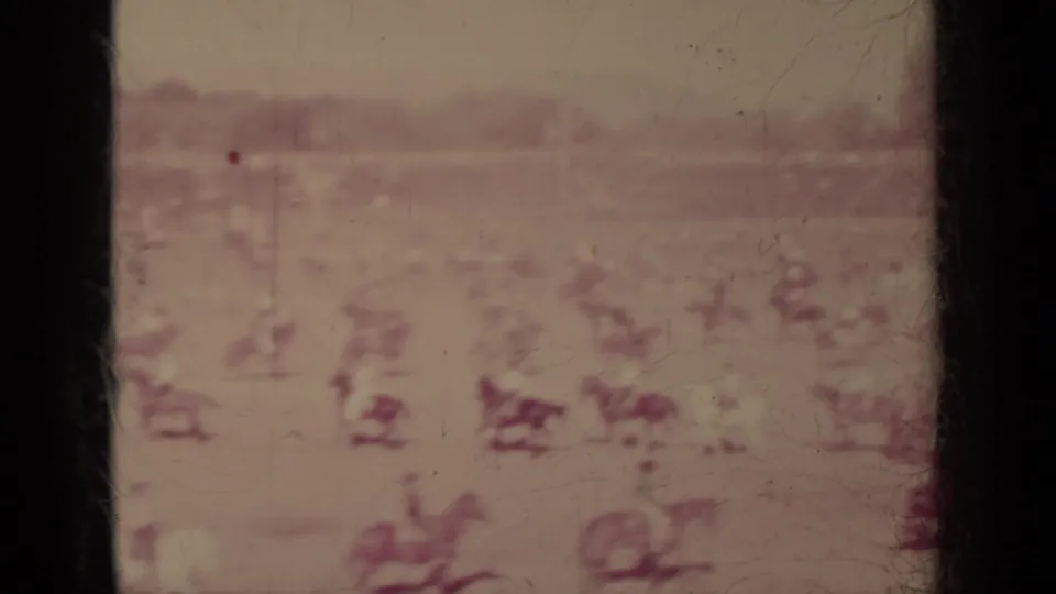 Wide, soft 8mm frame from Klamath, California showing distant horseback riders spread across an open field with low landscape beyond.