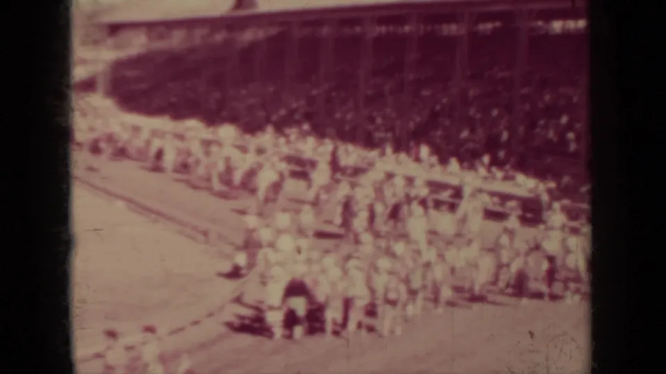 Faded 8mm frame from the Klamath racing event showing full stands and a group at the track edge.