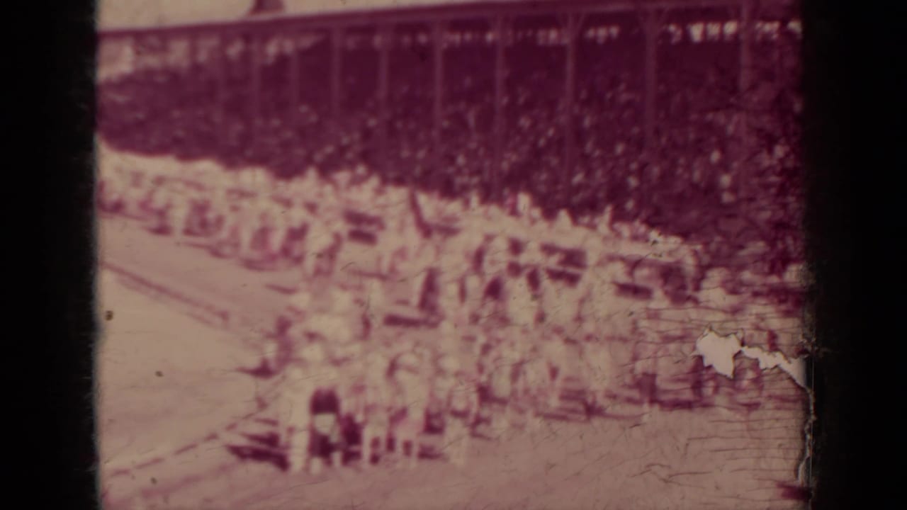 Distant parade marchers and riders pass bleachers filled with spectators.