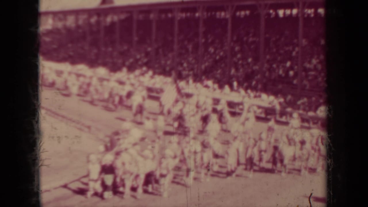 Distant 1937 Klamath parade view with marchers, possible flags, horseback riders, and spectators seated in background bleachers.