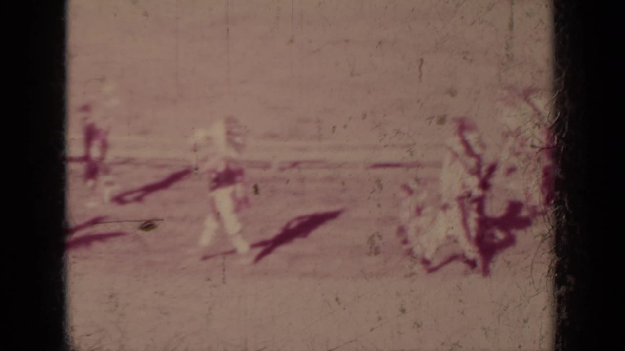 Faded 8mm frame from the Klamath parade showing scattered marchers and riders crossing a broad sunlit street.