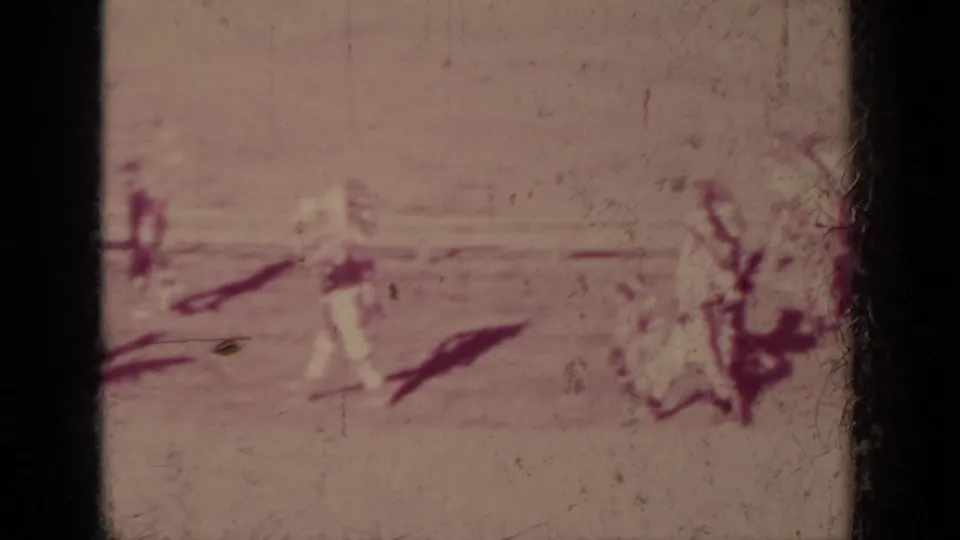 Faded 8mm frame from the Klamath parade showing scattered marchers and riders crossing a broad sunlit street.