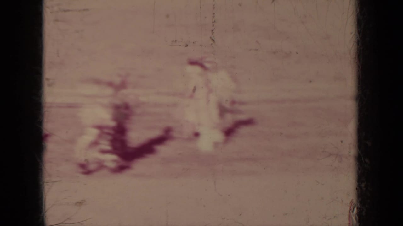 Soft, faded 1937 Klamath parade frame with riders and walkers moving across the street, seen through dark 8mm frame borders.