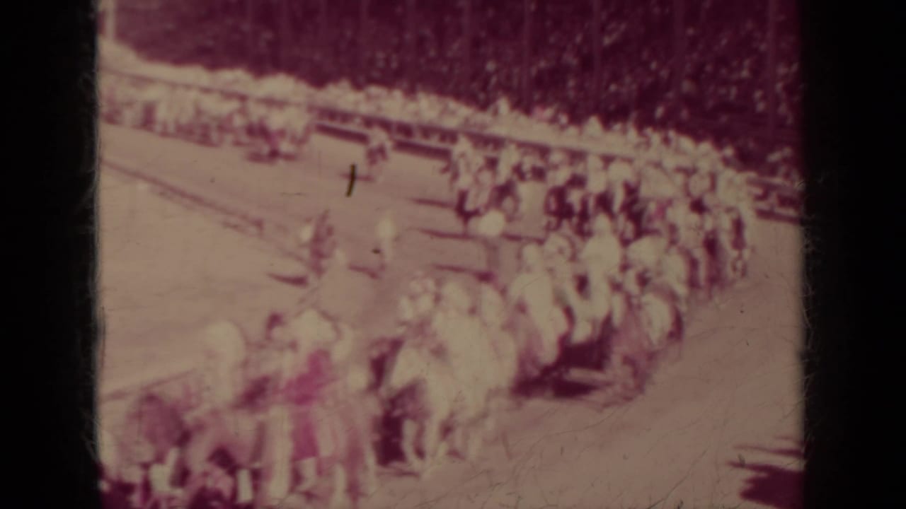 1937 Klamath, California 8mm frame showing a larger Indigenous horseback parade formation with clustered riders and flags.