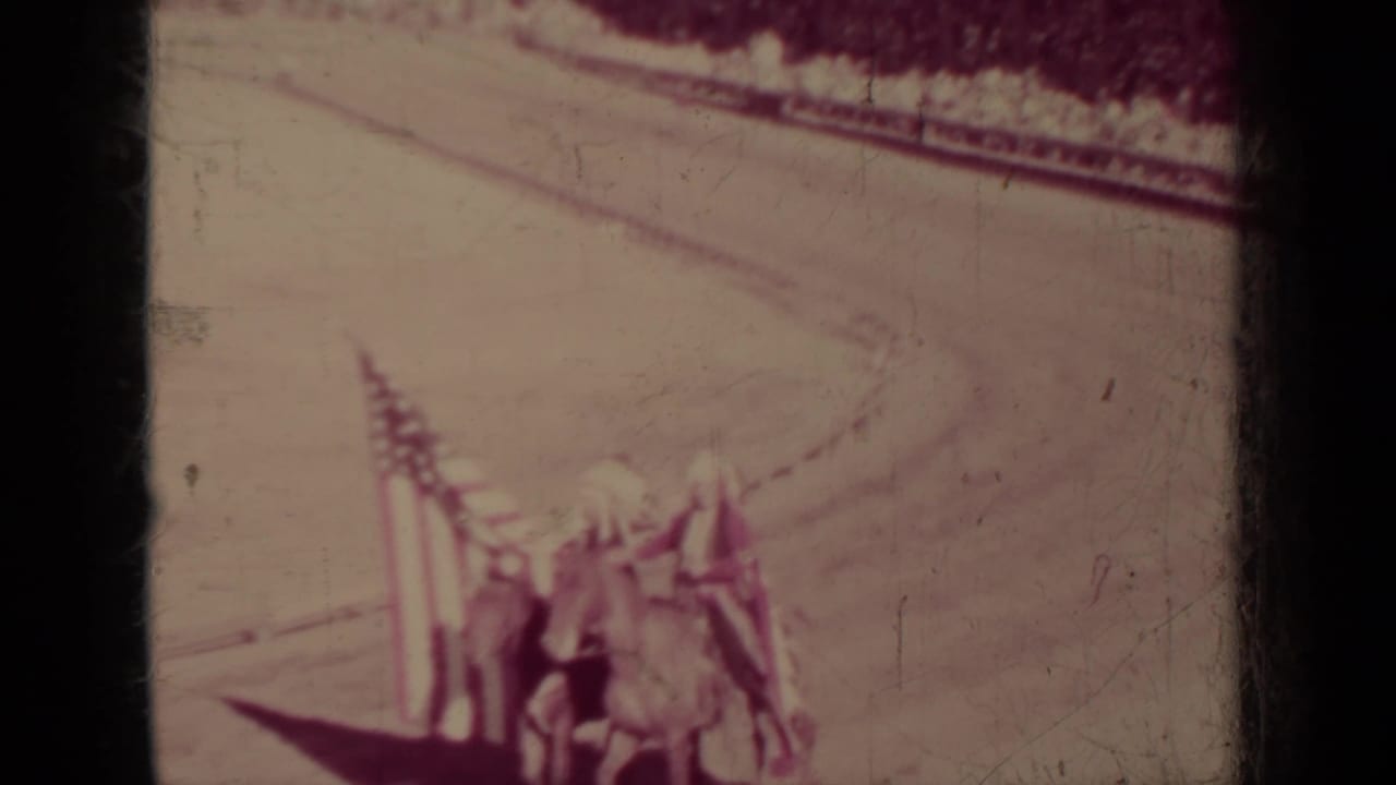 A Klamath, California parade frame shows horses and people near multiple flags, with a curved dirt track visible in the background.