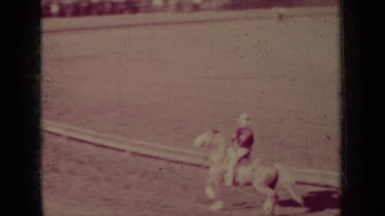 1937 Klamath home-movie frame showing a rider on a pale horse near curved tracks in an open arena.
