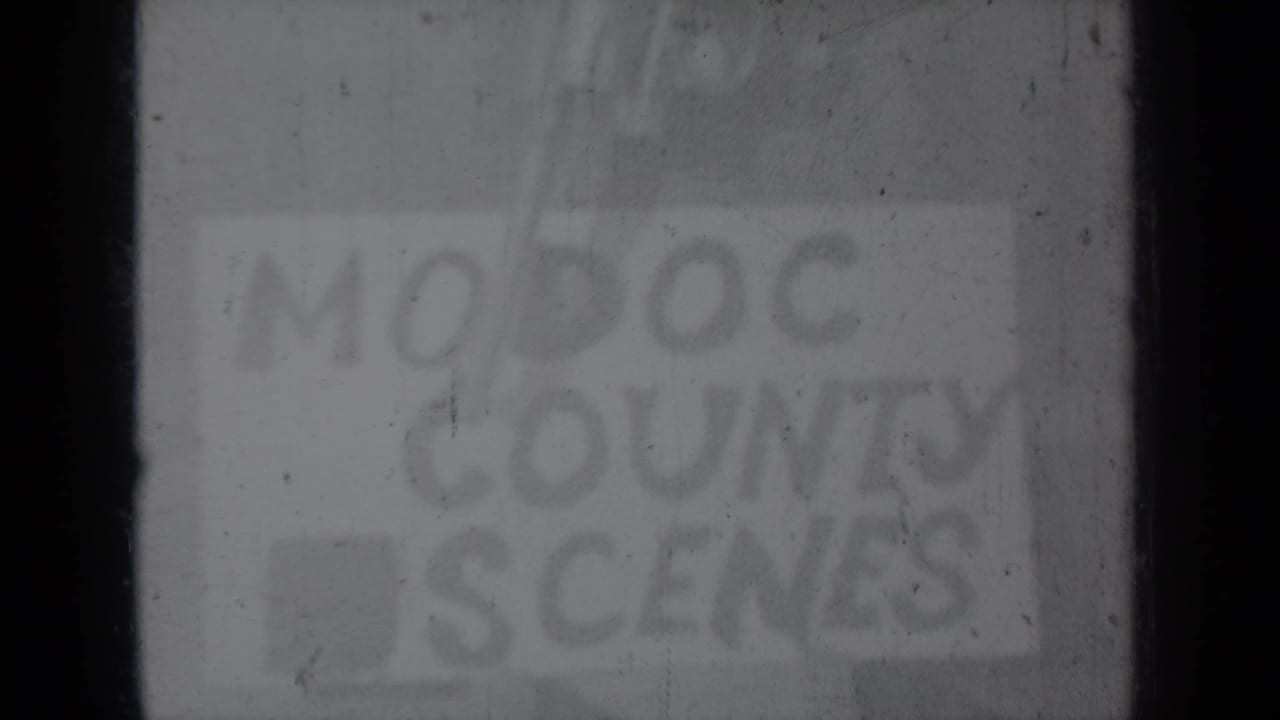 Final faded frame of the hand-lettered Modoc County title card, with heavy grain, scratches, and dark film edges.