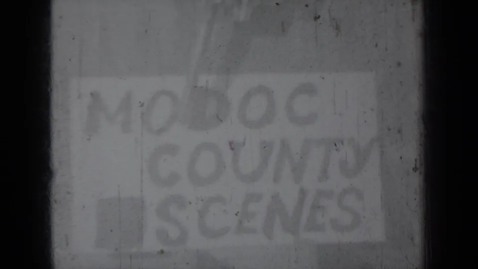 Faint black-and-white 1937 8mm frame showing a hand-lettered Modoc County Scenes card partly obscured by exposure and focus softness.
