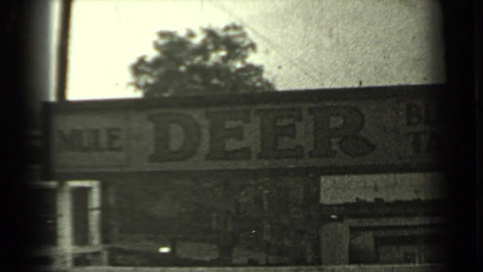 1937 Klamath-area home-movie frame showing a roadside Mule Deer Bar sign with trees above and heavy film-frame borders.