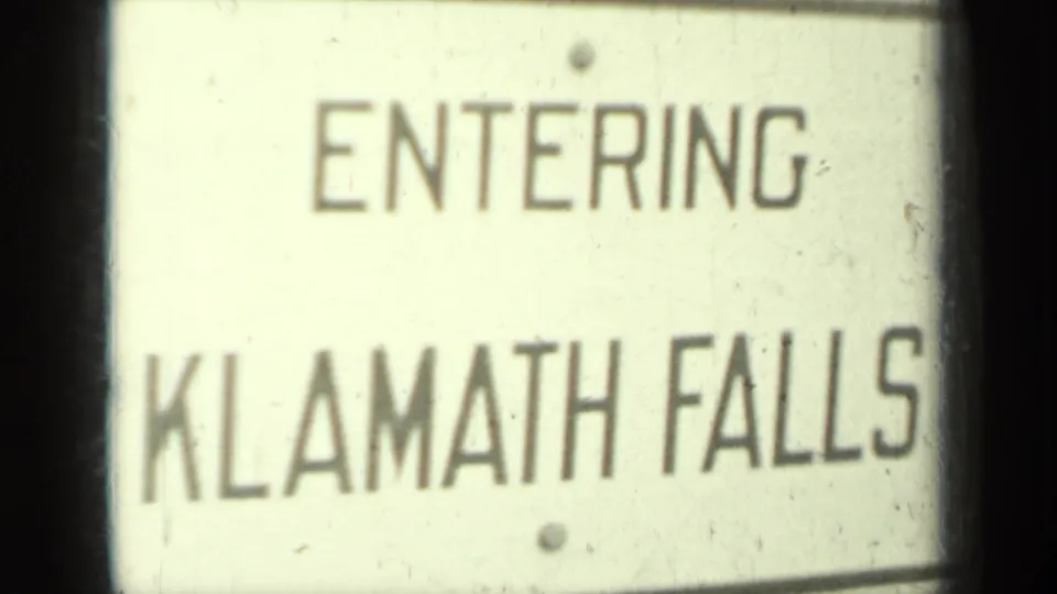 1937 home-movie view of an Entering Klamath Falls road sign, with dust marks and soft 8mm exposure visible.