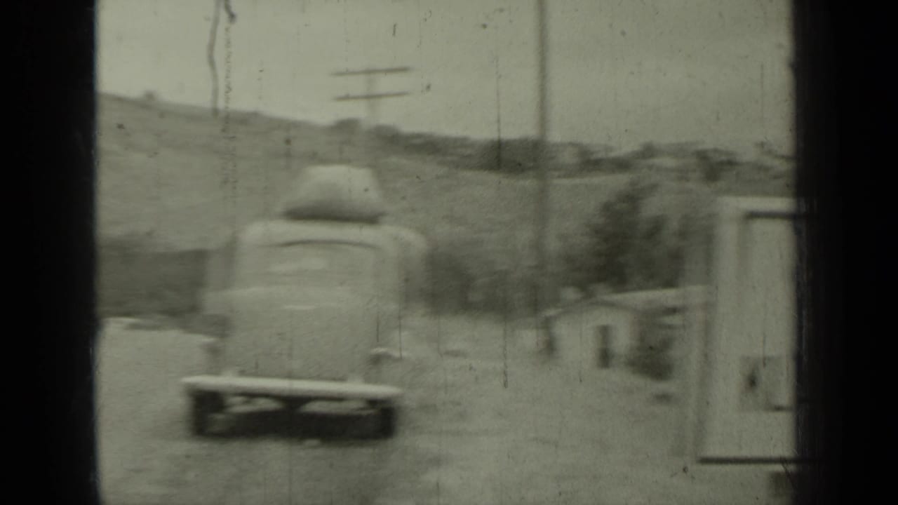 Car with roof luggage driving away on a road near low hills.