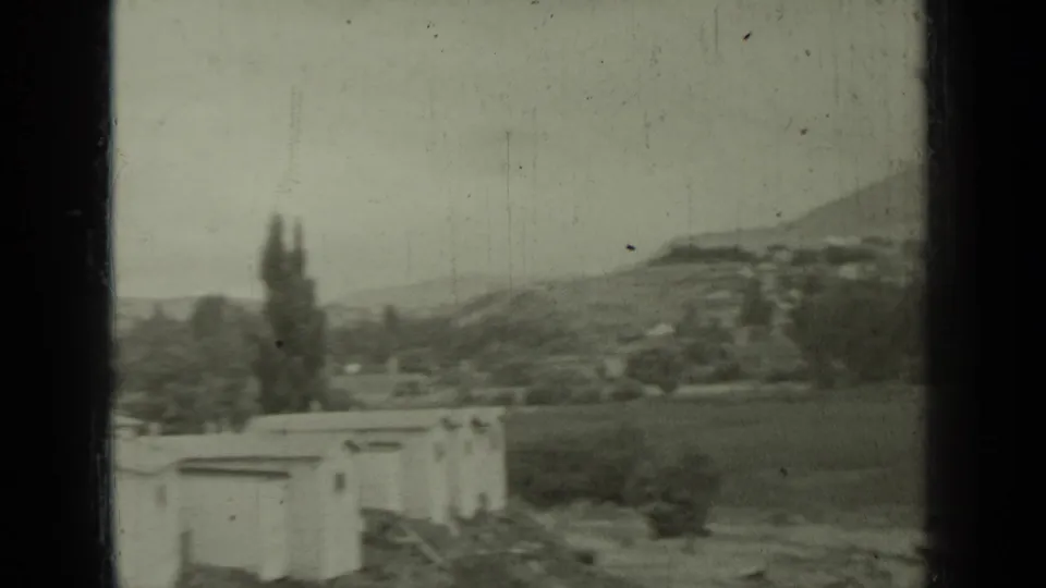 1937 8mm frame looking across open fields, small roadside structures, trees, and hills during the approach to Klamath Falls in California.
