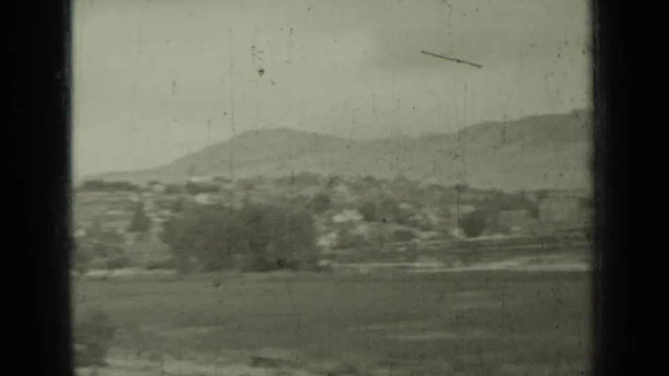 1937 8mm frame showing open land, distant buildings, trees, and mountain slopes near Klamath Falls, California, from a moving travel viewpoint.