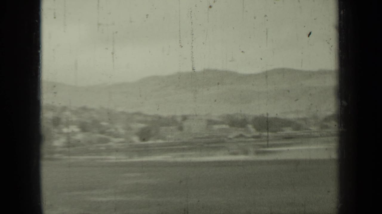 1937 Klamath-area coastal landscape seen from a moving vehicle, with hills, water, shoreline, and window bars in view.