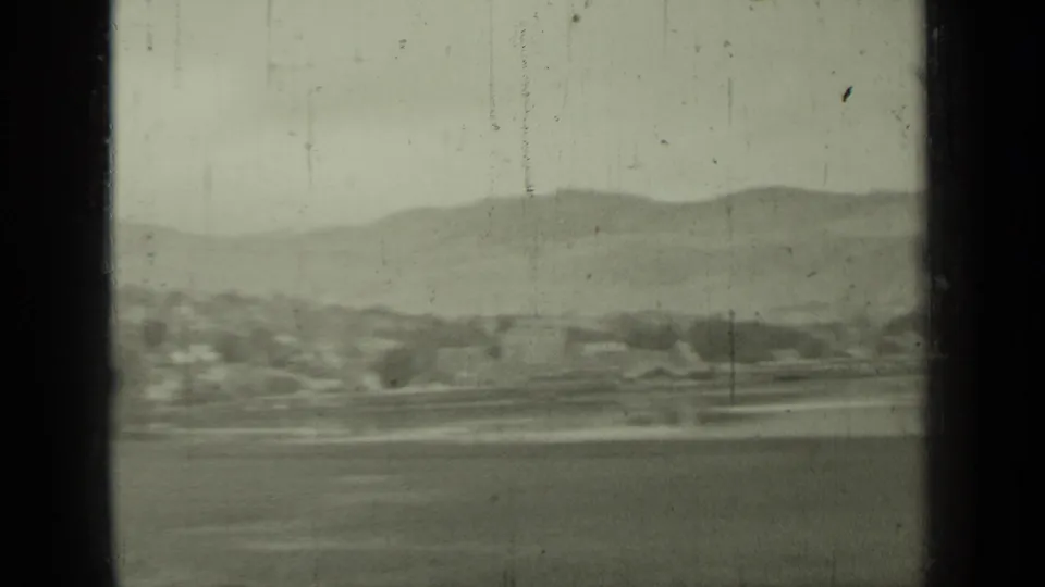 1937 Klamath-area coastal landscape seen from a moving vehicle, with hills, water, shoreline, and window bars in view.