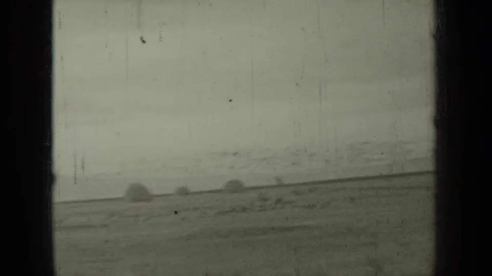 1937 Klamath, California 8mm frame showing a blurred rural field, faint roadside or track line, and rounded dark shapes in the distance.