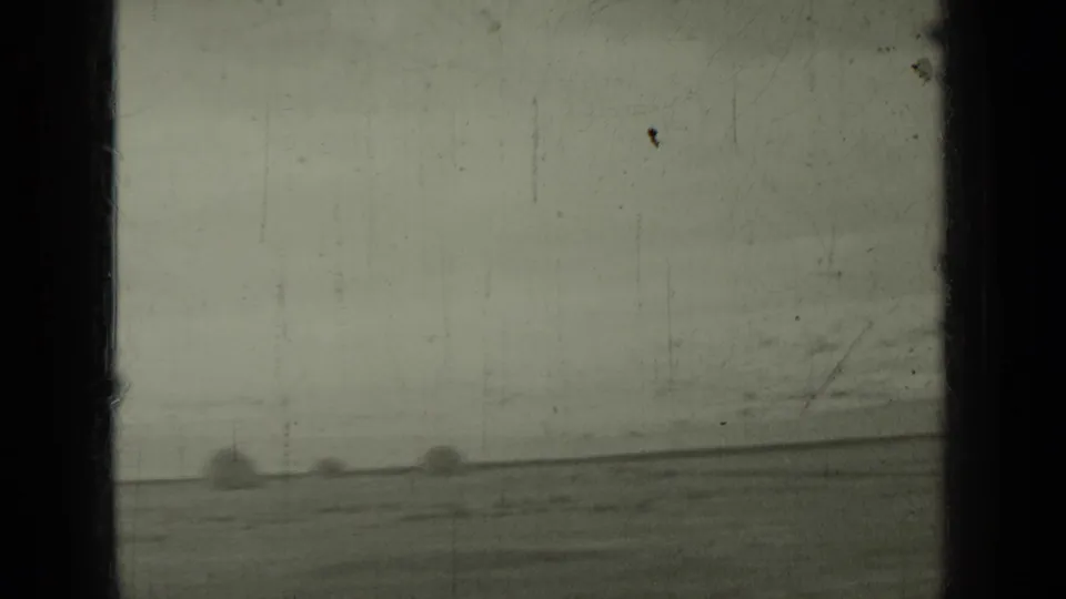 1937 Klamath, California 8mm frame showing a muted open field, distant hay bales, and dark vertical framing at the edges.