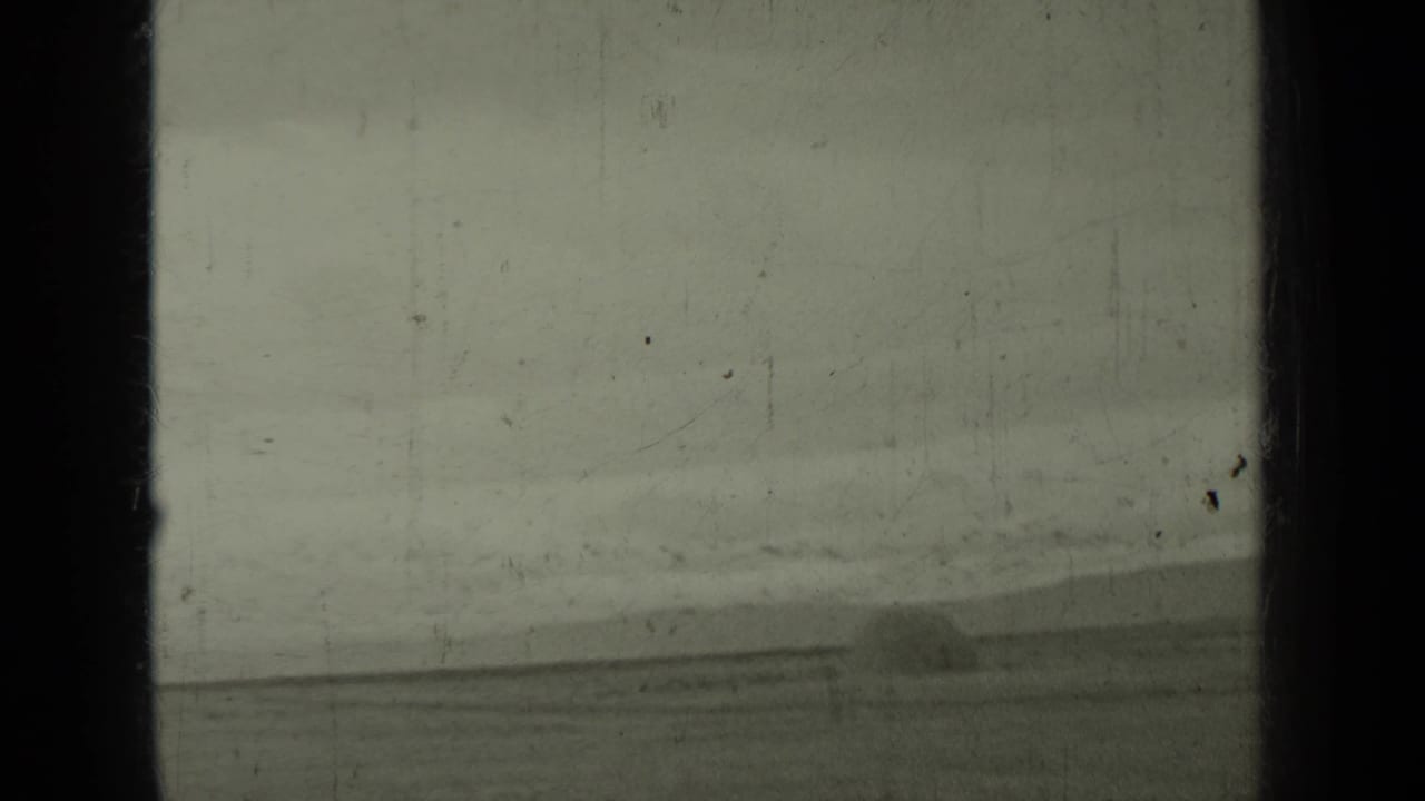 Distant railroad tracks run through a hilly landscape with a steam train barely visible ahead.