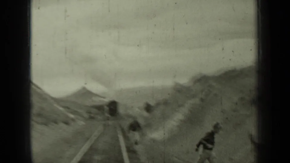 1937 Klamath, California frame with an approaching steam train, smoke, rocky embankment, and a person near the tracks.