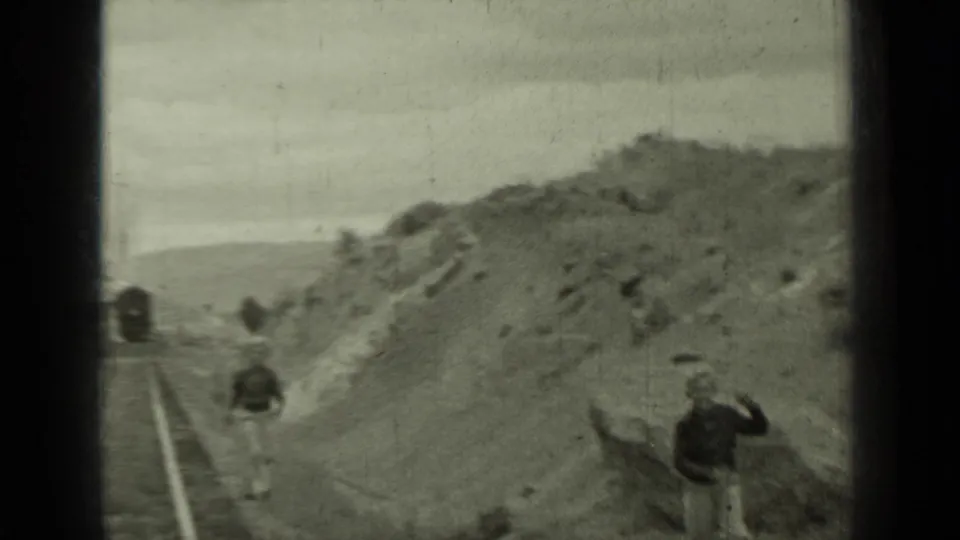1937 Klamath, California home-movie frame showing young people near tracks, a distant train, and rough hillside terrain.