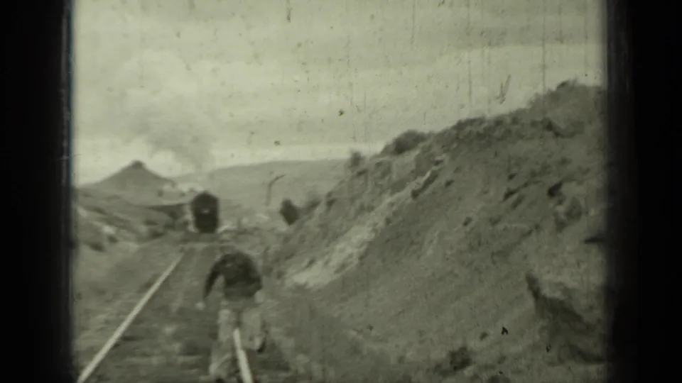 1937 Klamath, California frame with a person close to the rail, an approaching steam train, smoke, and rocky slopes.