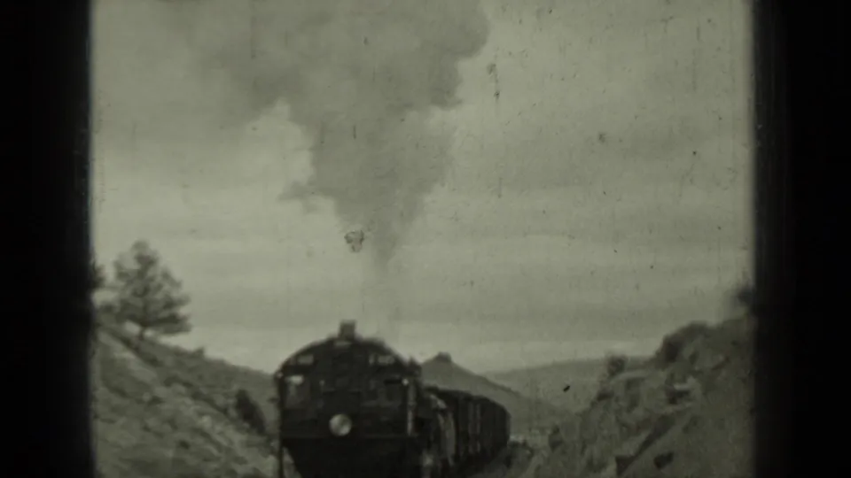 1937 Klamath, California 8mm frame showing a steam locomotive approaching through a rural hillside rail cut.