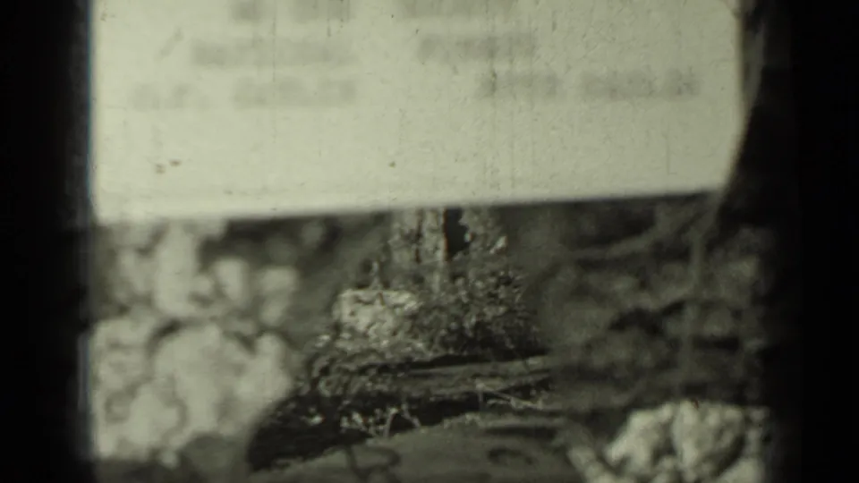 Soft 8mm frame from the Klamath travel clip showing a pale sign or board partly obscured by brush and film-gate shadow.