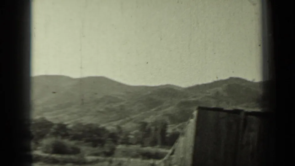 1937 Klamath, California 8mm frame showing distant hills through a window frame, with a rough fence and trees in the foreground.