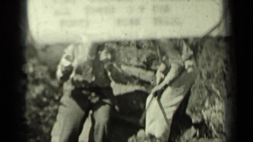 Two adult men in 1930s outdoor clothing stand near a rough stone wall in the supplied Klamath, California home-movie footage.
