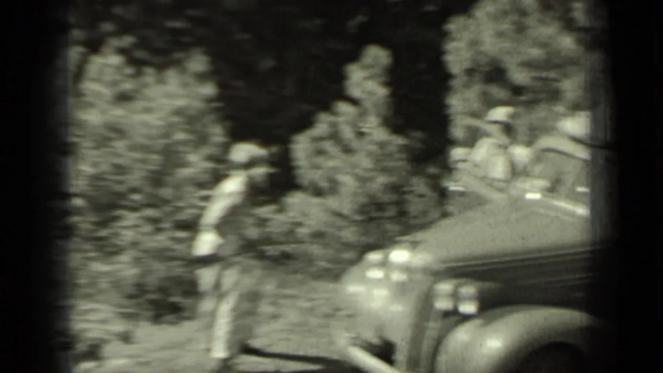 1937 Klamath, California home-movie frame showing a sedan stopped on a wooded road with people positioned near the vehicle.
