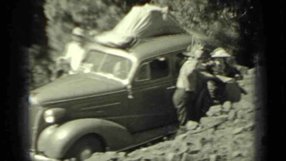 1937 Klamath, California home-movie frame showing people beside a sedan while a man appears to point a firearm near the group.