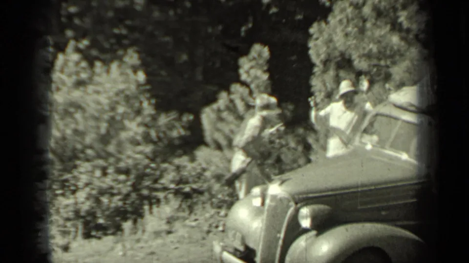 1937 Klamath, California frame showing adults near a sedan in a wooded roadside setting, with period clothing and hats visible.