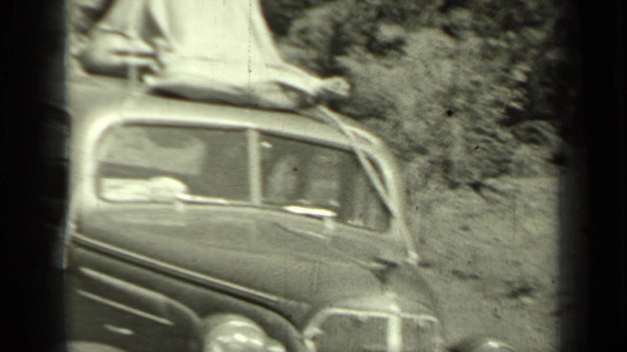 1930s sedan parked near trees with canvas or tent material strapped to the roof.