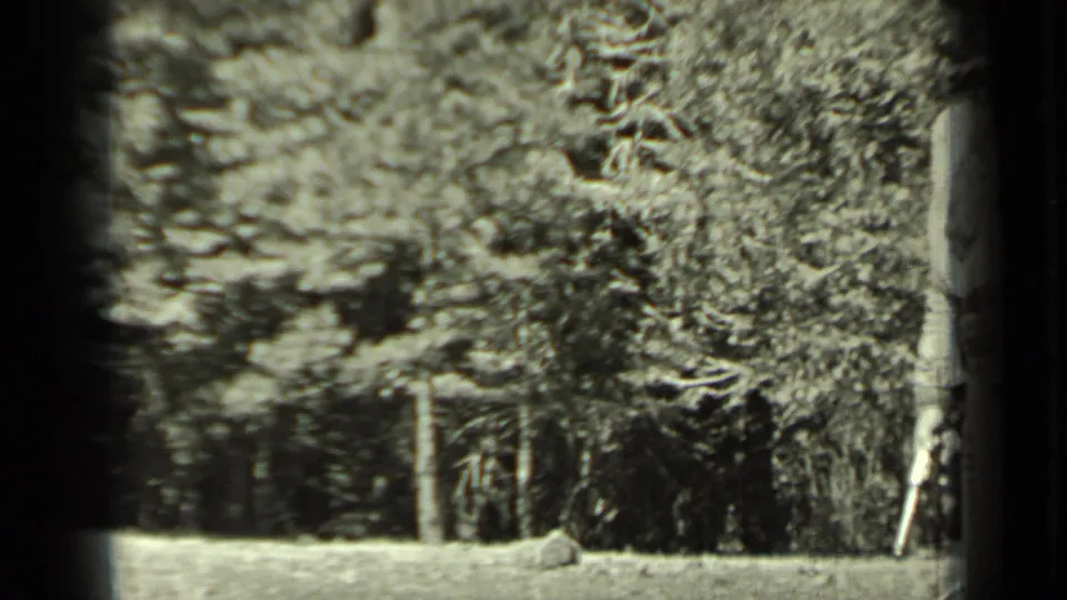 Black-and-white 1937 Klamath home-movie frame showing two boys on a grassy wooded slope, partly obscured by dark film edges.
