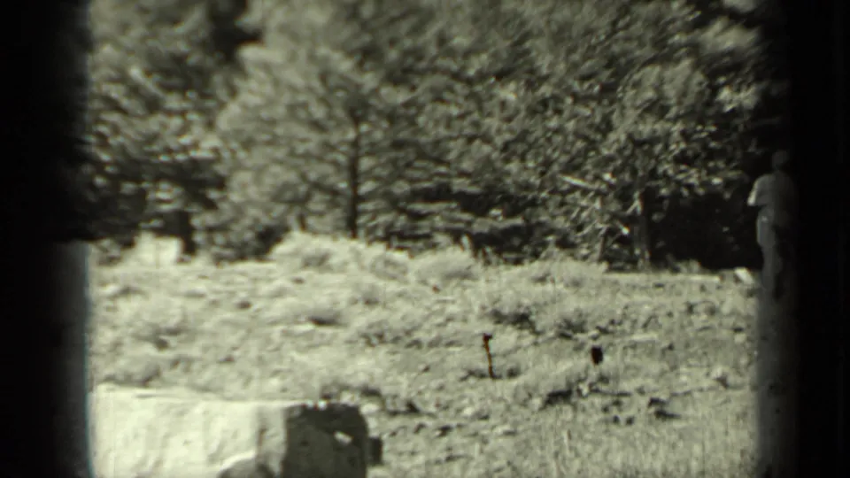 Black-and-white 1937 Klamath frame with a boy near a tree line, holding a long stick-like or toy-gun object beside the hillside.