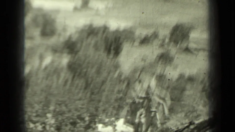 Motion-blurred black-and-white home-movie frame of a boy moving through grassy brush on a rural Klamath hillside.