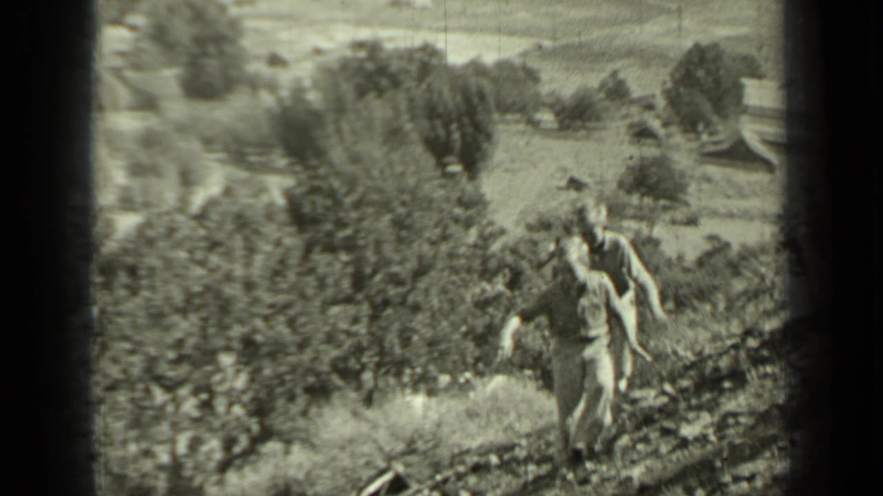 Two young people run up a hillside with fields and trees behind them.