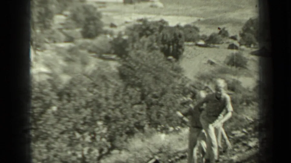 Two young people move uphill through a rural Klamath, California landscape in soft black-and-white 8mm footage.