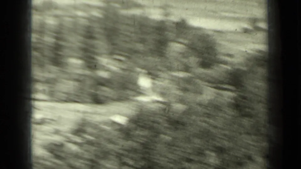 A blurred black-and-white frame shows hillside vegetation and open ground during quick handheld movement in the home movie.