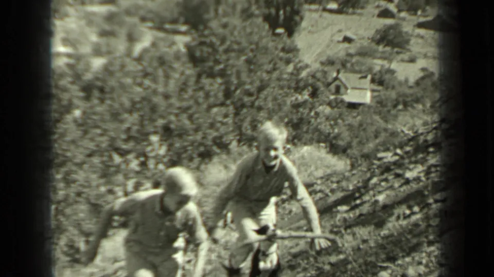 Two young people near the camera on a rural hillside, with trees and small distant structures visible in Klamath, California.