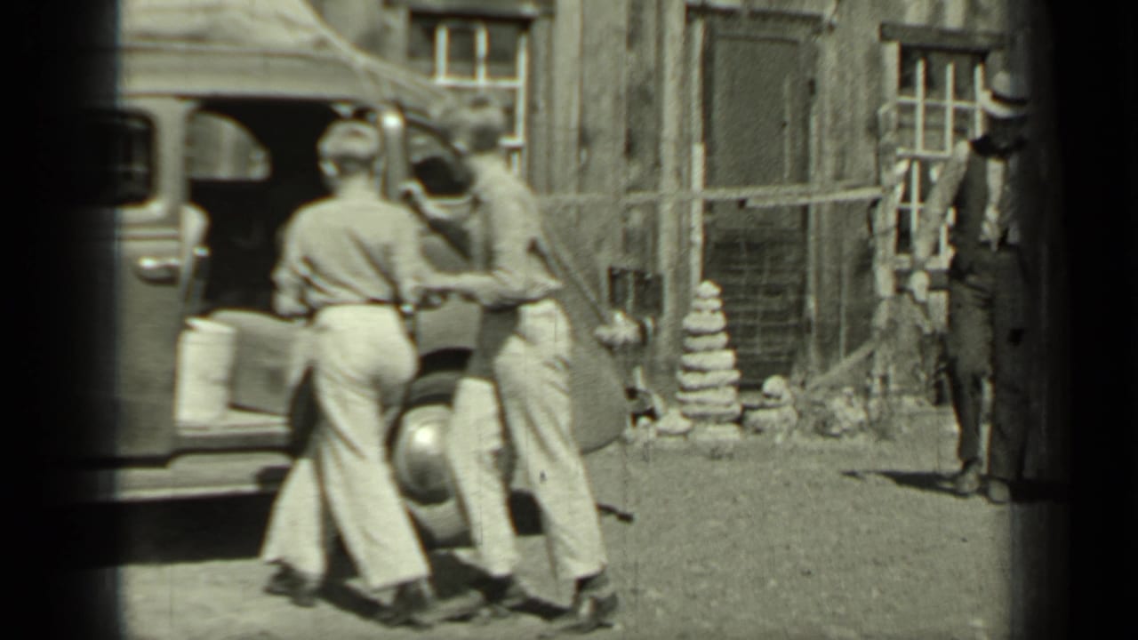 Two young people appear to hop into or lean into a 1930s sedan in Klamath, with a man standing near the wood-sided building behind them.