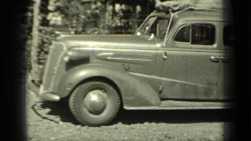 1937 Klamath, California home-movie frame showing a packed vintage sedan on gravel with roof luggage and rounded front fender.