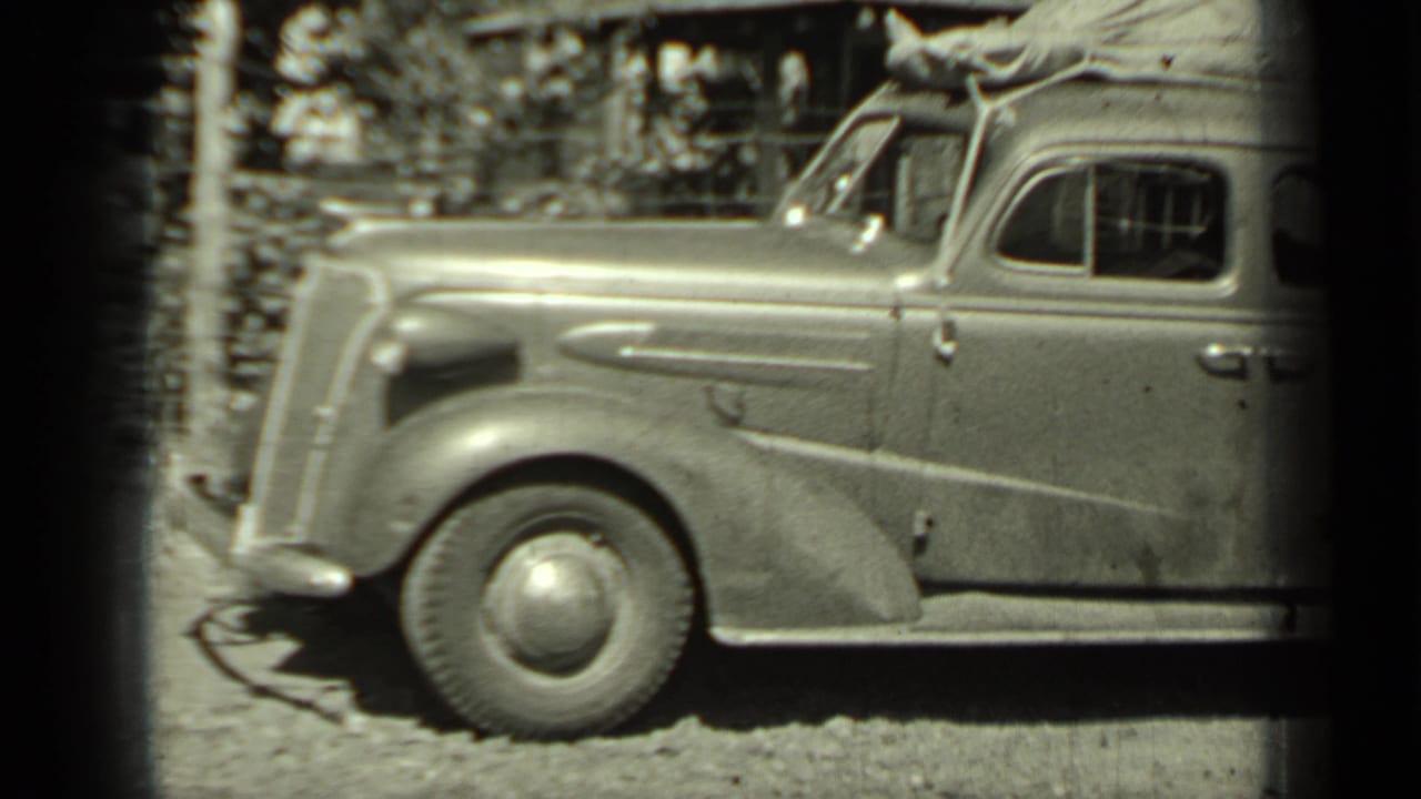 A vintage sedan in Klamath, California, appears loaded for travel, with roof luggage, rounded fenders, and a gravel roadside setting.