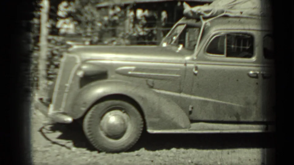 A vintage sedan in Klamath, California, appears loaded for travel, with roof luggage, rounded fenders, and a gravel roadside setting.