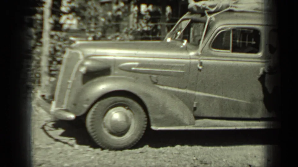 Black-and-white 8mm frame of a 1930s sedan in Klamath, California, showing the front wheel, side panel, and luggage on the roof.