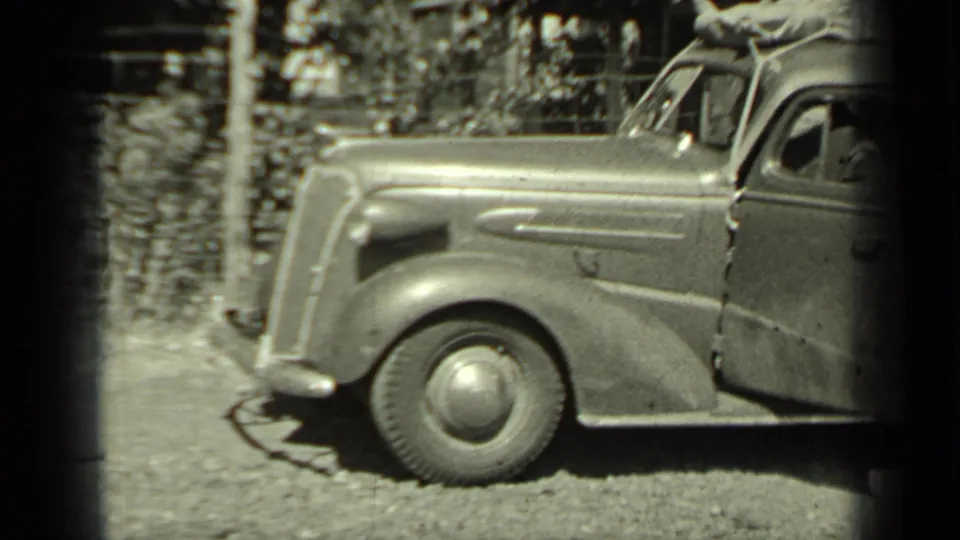 The packed sedan remains parked on gravel, with a partial figure visible at the passenger-side edge of the 1937 Klamath home-movie frame.