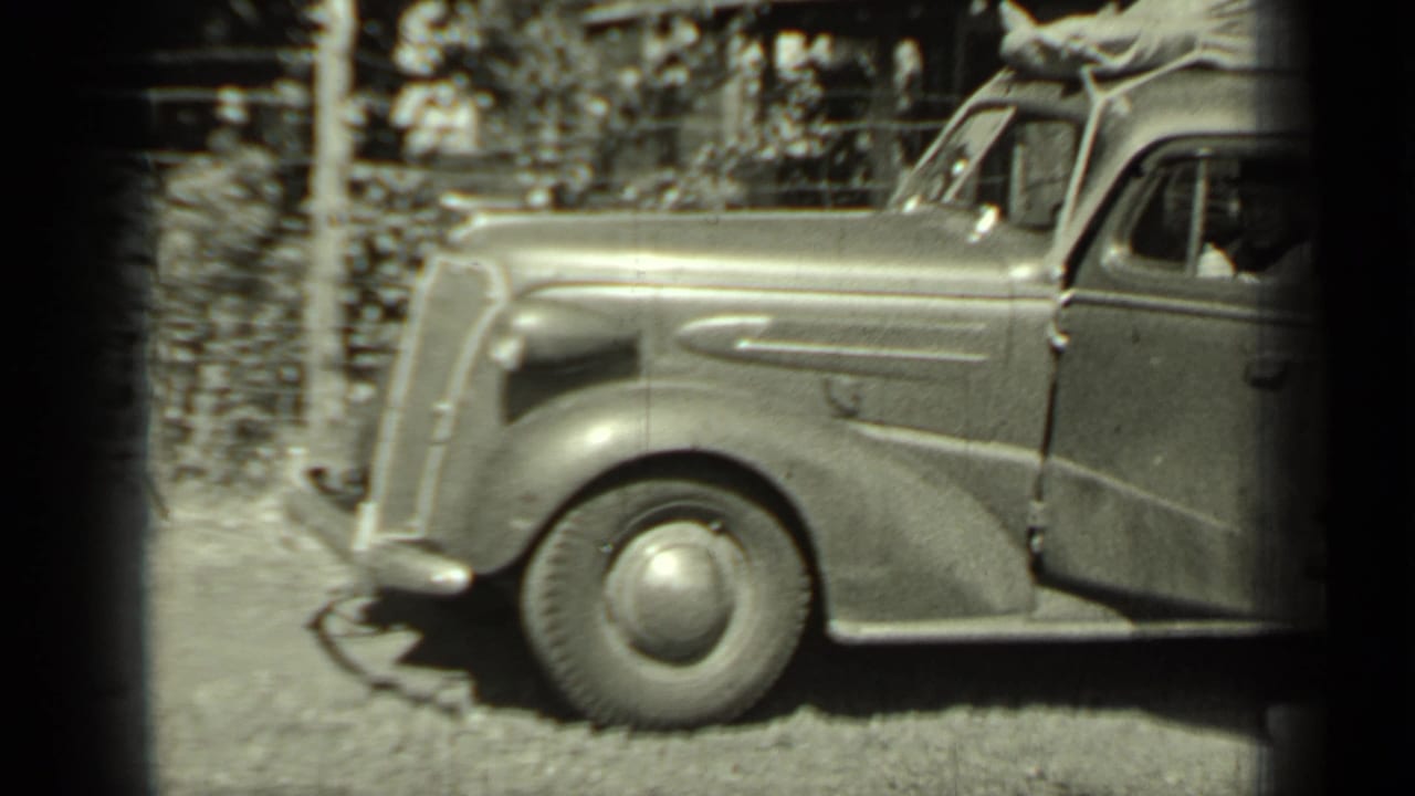 Vintage car parked on a dirt road beside a wooden fence.