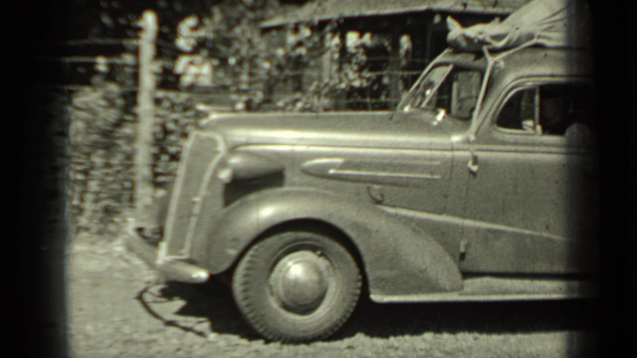 Front half of a vintage automobile near a fence and trees.