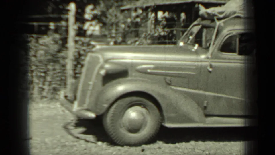 1937 Klamath, California footage frame showing a vintage automobile's front section beside a wooden fence and roadside vegetation.